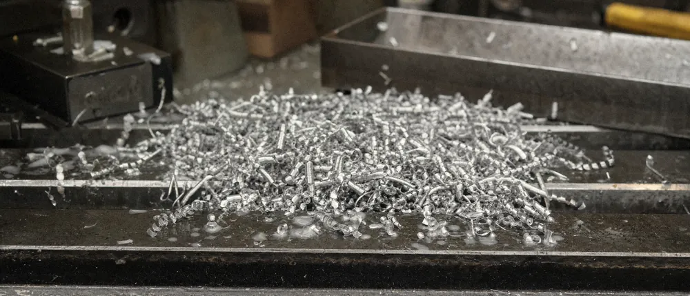 A heap of curled aluminium chips and drops of coolant on a steel machine table.